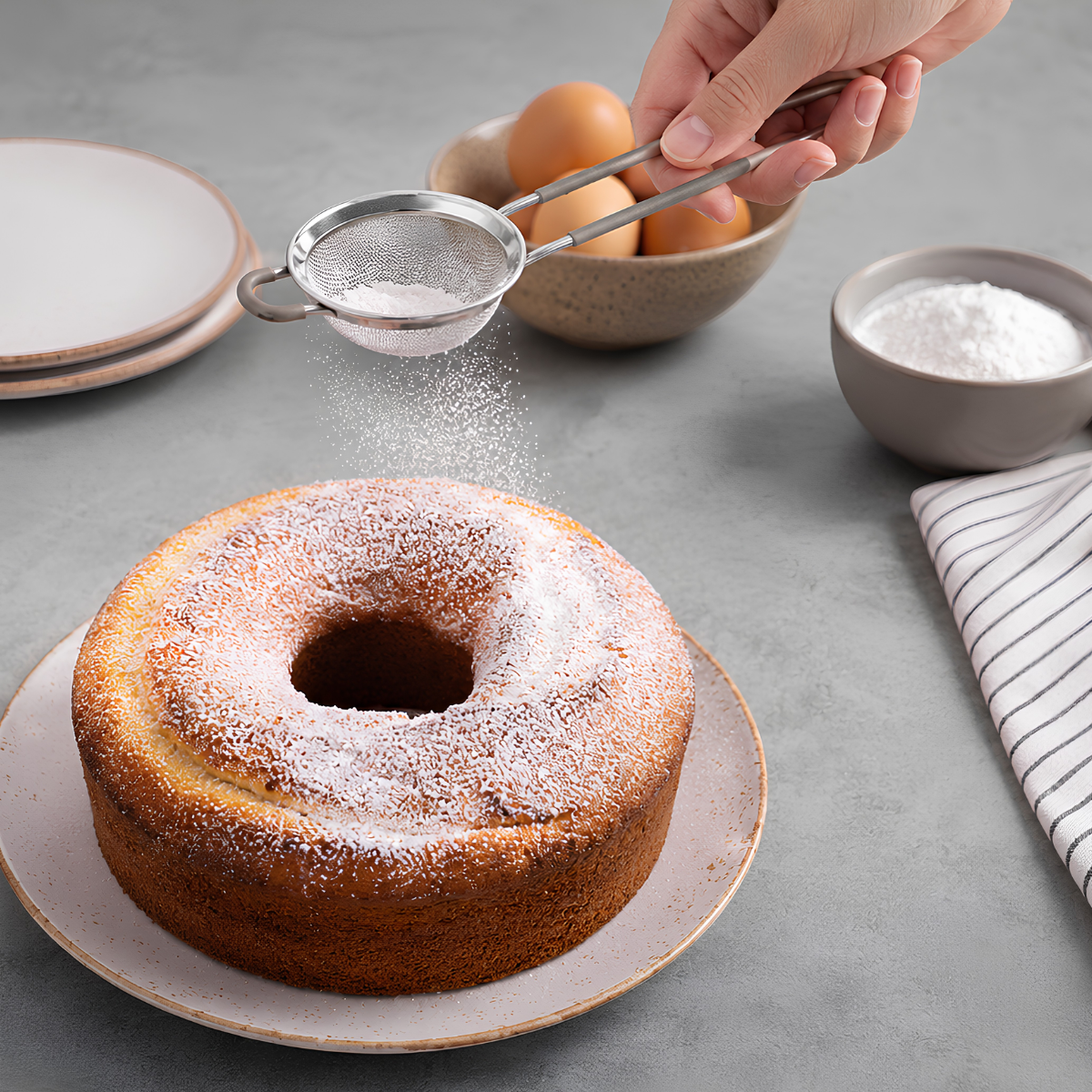 Handheld stainless steel sieve with grey silicone grip over powdered sugar