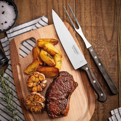 Brown cutting board with grilled steak, roasted pieces, and stainless barbecue knives
