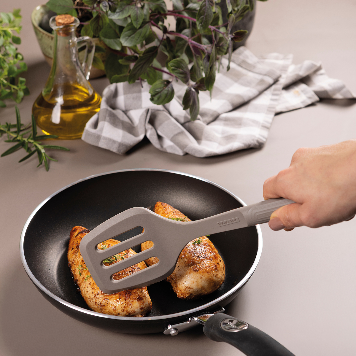 Grey silicone slotted spatula lifting food from a nonstick pan