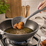 Grey silicone slotted skimmer lifting food from frying pan.