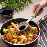 Grey silicone serving spoon lifting food from a skillet