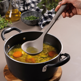Grey silicone ladle scooping soup from a pot, rounded bowl and long handle