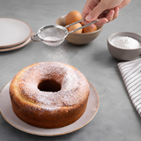 Handheld stainless steel sieve with grey silicone grip over powdered sugar