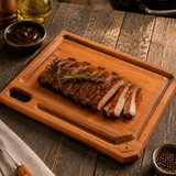 Brown wooden board with groove holding sliced steak and rosemary.