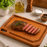 Brown wooden board with groove holding sliced steak and herbs.