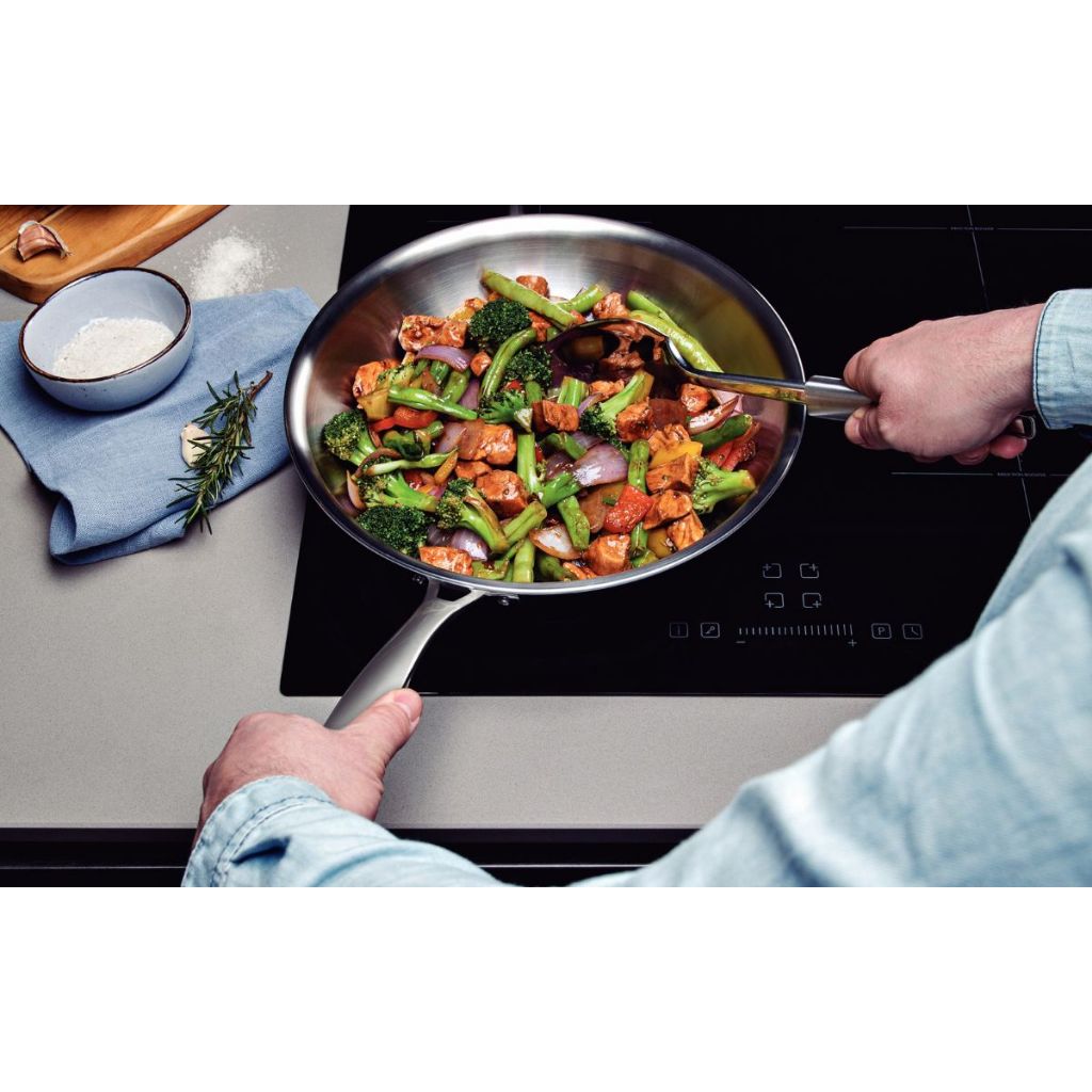 Stainless steel skillet on induction cooktop with sautéed vegetables and meat